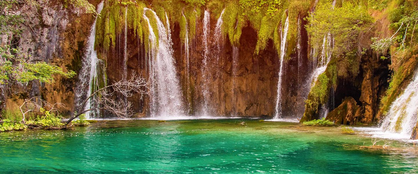 Beautiful pool of water with streams of water cascading over lush greenery and cliffs